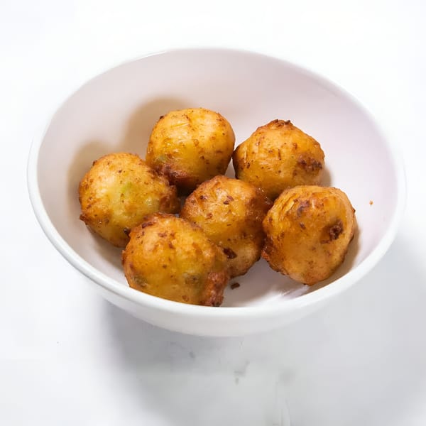 Six golden-brown, fried hushpuppies are served in a white bowl on a white background.