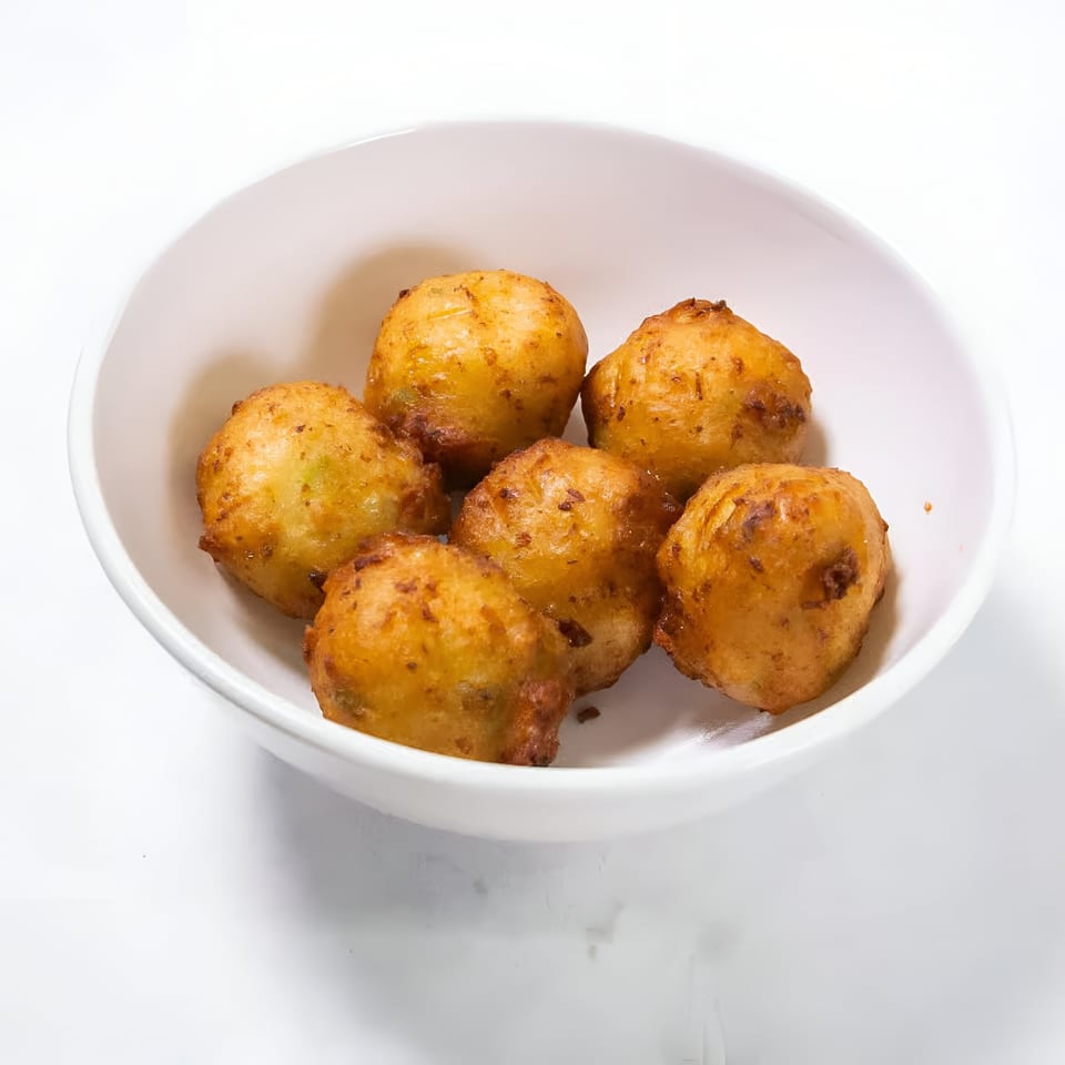 Six golden-brown, fried hushpuppies are served in a white bowl on a white background.