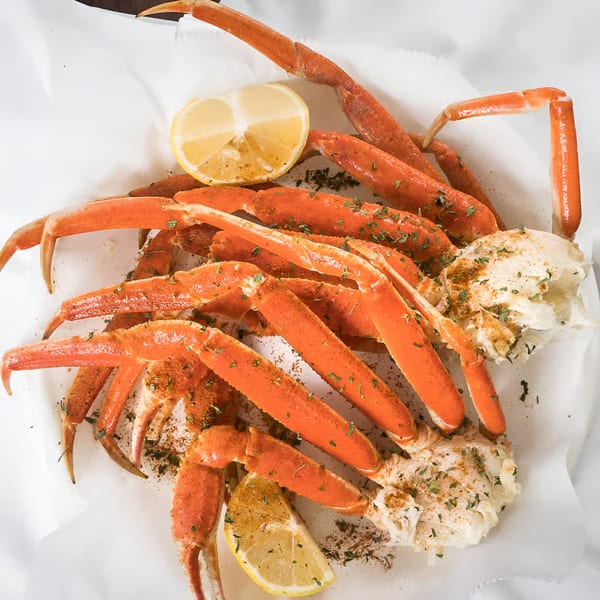 Quickie's Burgers, Wings & Seafood snow crab legs with lemon wedges and seasoning on white paper.