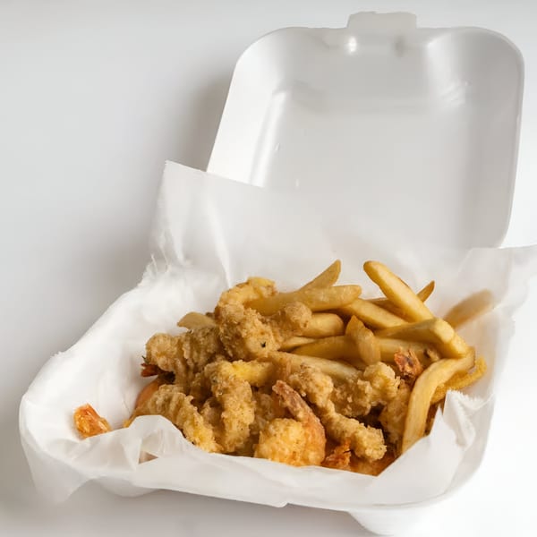 Fried shrimp and french fries in a white styrofoam takeout container with a white paper liner.