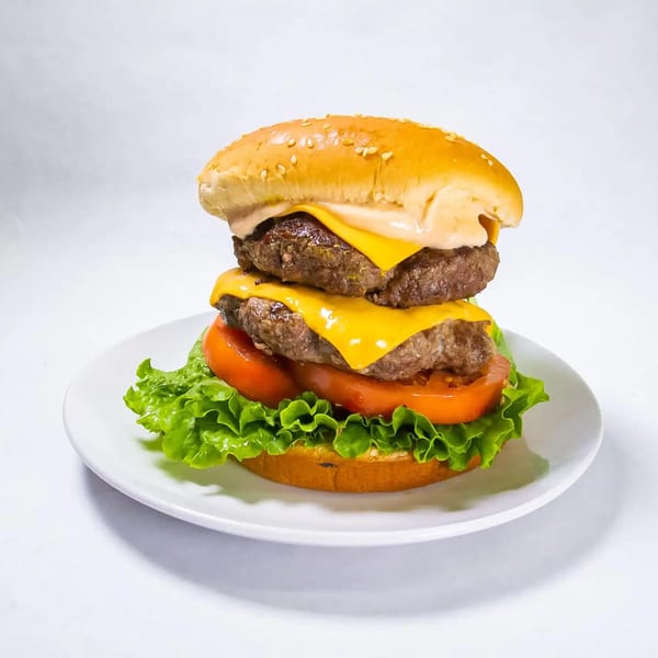 A double cheeseburger with lettuce, tomato, and sauce on a white plate.
