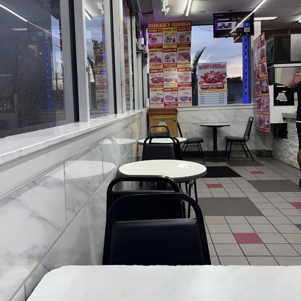 Interior of Quickie's Burgers, Wings & Seafood with empty tables, chairs, and menu boards visible.