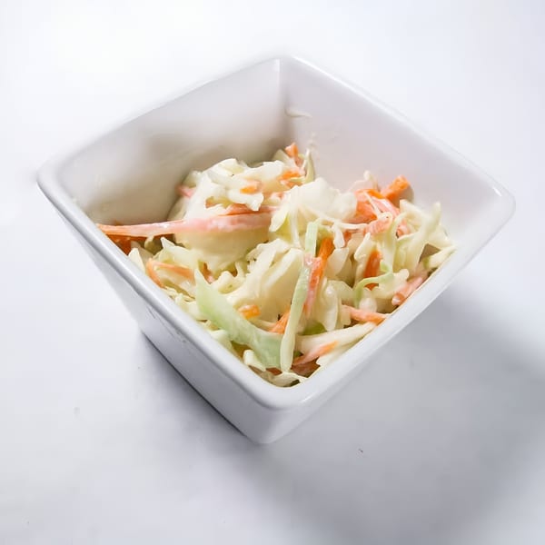 Creamy coleslaw with shredded cabbage and carrots in a white square bowl.