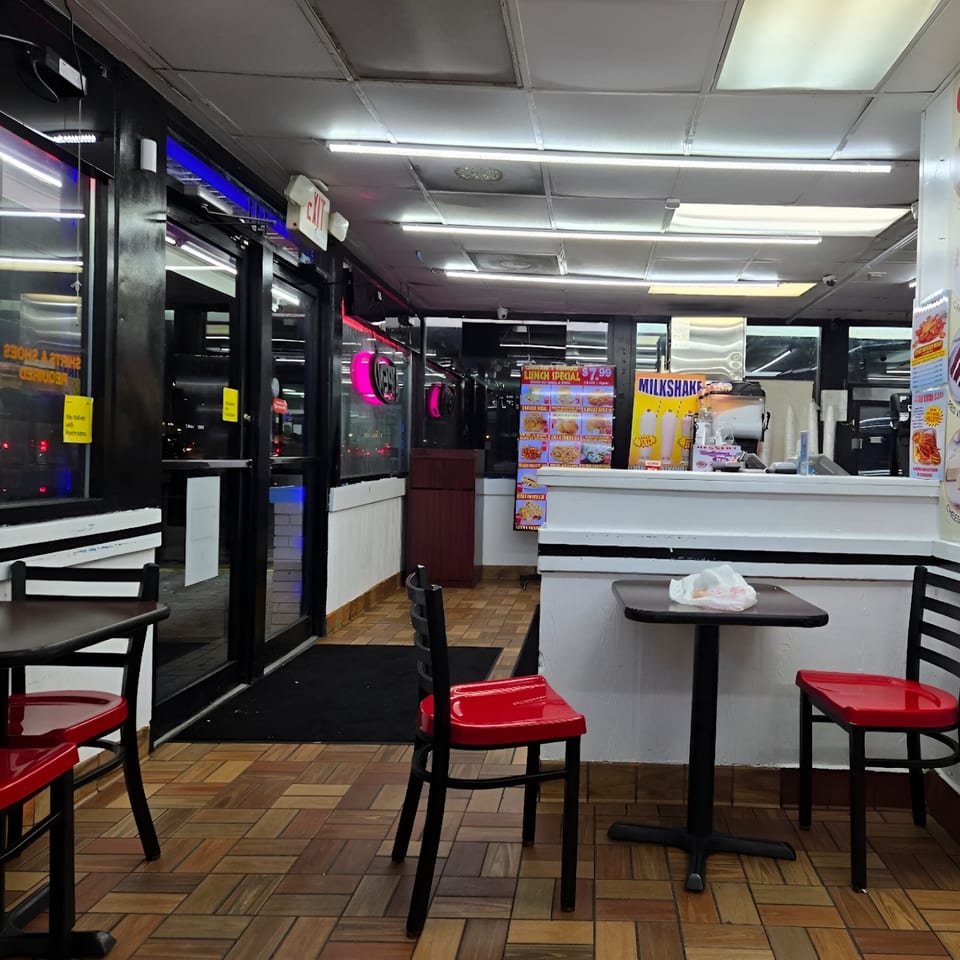 Interior of Quickie’s Burgers, Wings & Seafood, featuring red chairs, dark tables, and menu boards.
