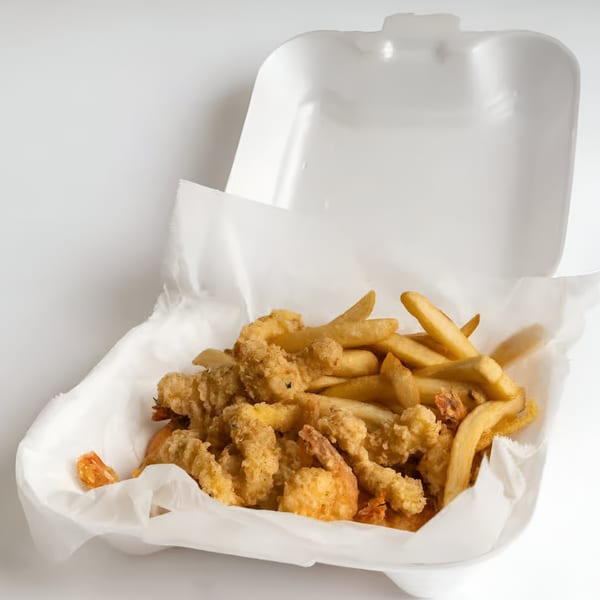 Quickie’s fried shrimp and french fries in a white takeout container with a paper liner.