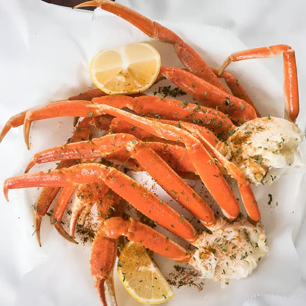 Quickie’s Burgers, Wings & Seafood snow crab legs with lemon wedges and seasoning on white paper.