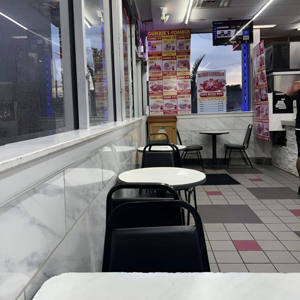 Interior of Quickie's Burgers, Wings & Seafood with empty tables, chairs, and menu boards.