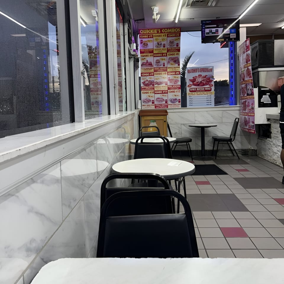 Interior of Quickie's Burgers, Wings & Seafood with empty tables, chairs, and menu boards.