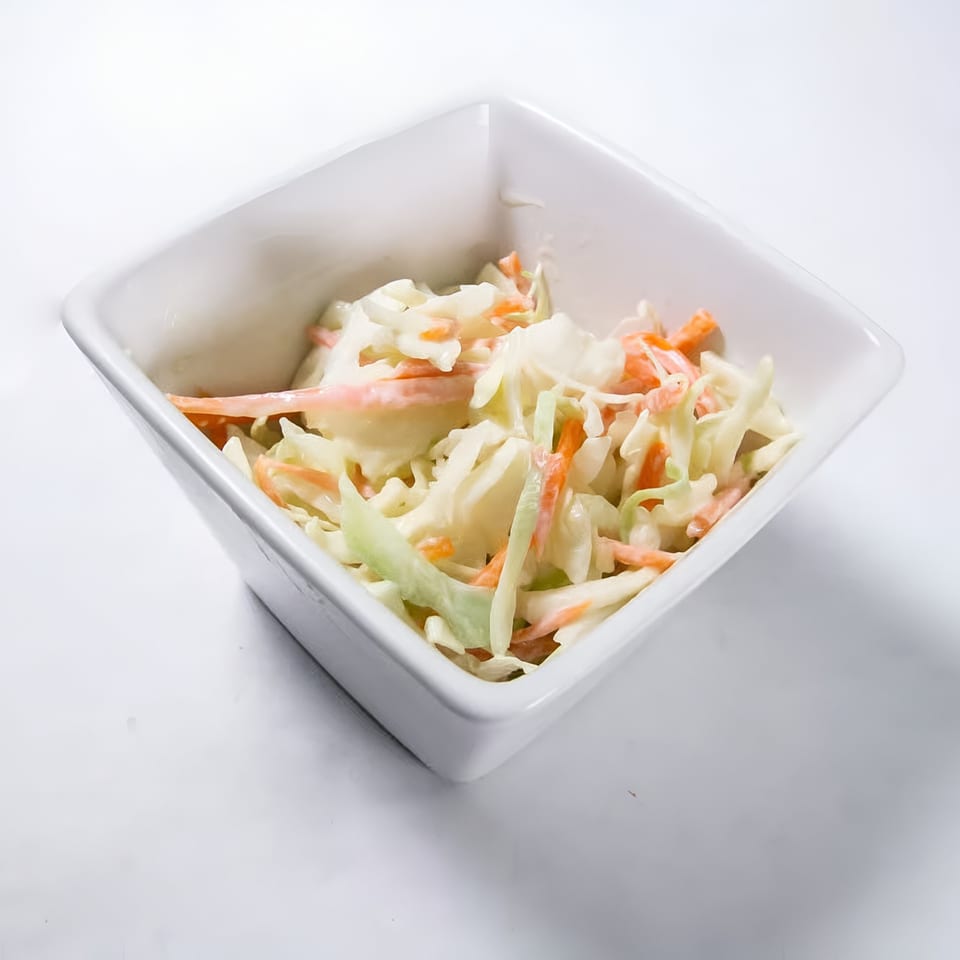 Creamy coleslaw with shredded cabbage and carrots in a white square bowl.