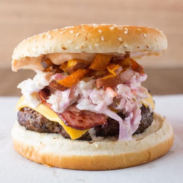 A Quickie's burger with a beef patty, cheese, bacon, coleslaw, and sweet potato fries.
