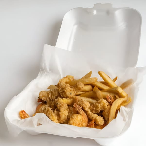 Fried shrimp and french fries in a white styrofoam takeout container lined with paper.