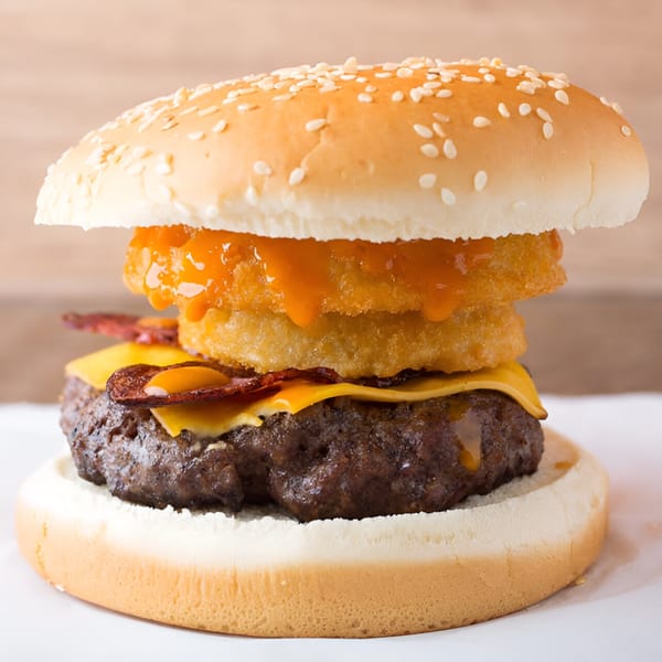 Quickie’s Burger with a beef patty, melted cheese, bacon, and onion rings with sauce.