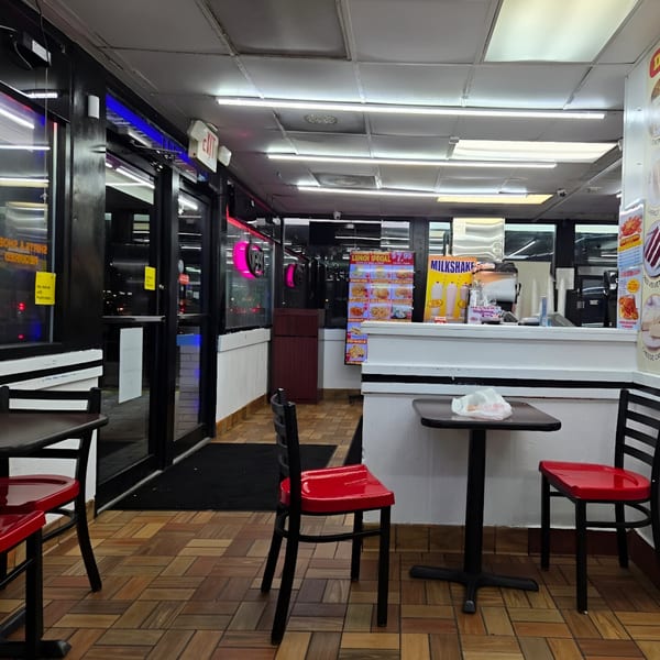 Interior of Quickie’s Burgers, Wings & Seafood, showing empty tables, red chairs, and a service counter.