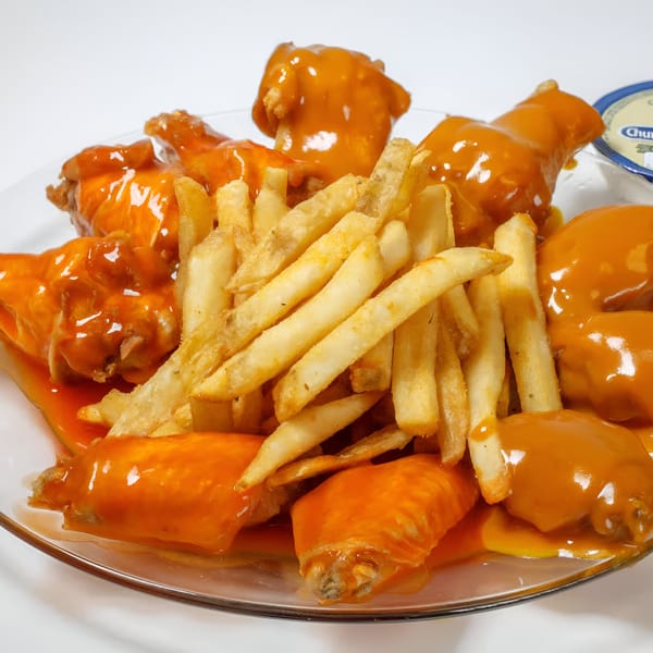 Quickie’s Burgers, Wings & Seafood's buffalo wings and french fries on a clear plate.