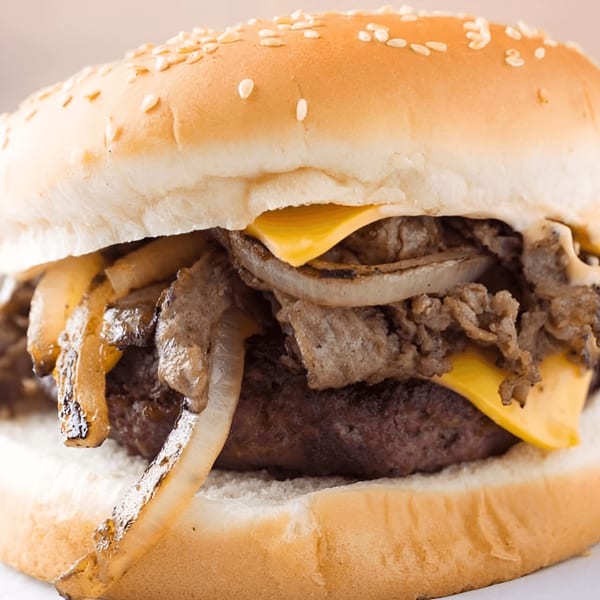 Close-up of a Quickie's burger with a patty, melted cheese, and grilled onions on a sesame bun.