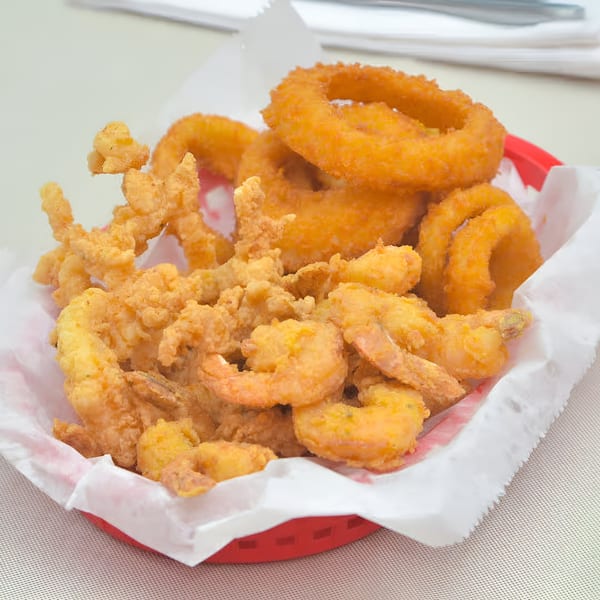 A red basket filled with golden-brown fried shrimp, clams, and onion rings from Quickie's Burgers, Wings & Seafood.
