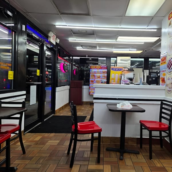Interior of Quickie’s Burgers, Wings & Seafood, showing empty tables, red chairs, and a service counter.
