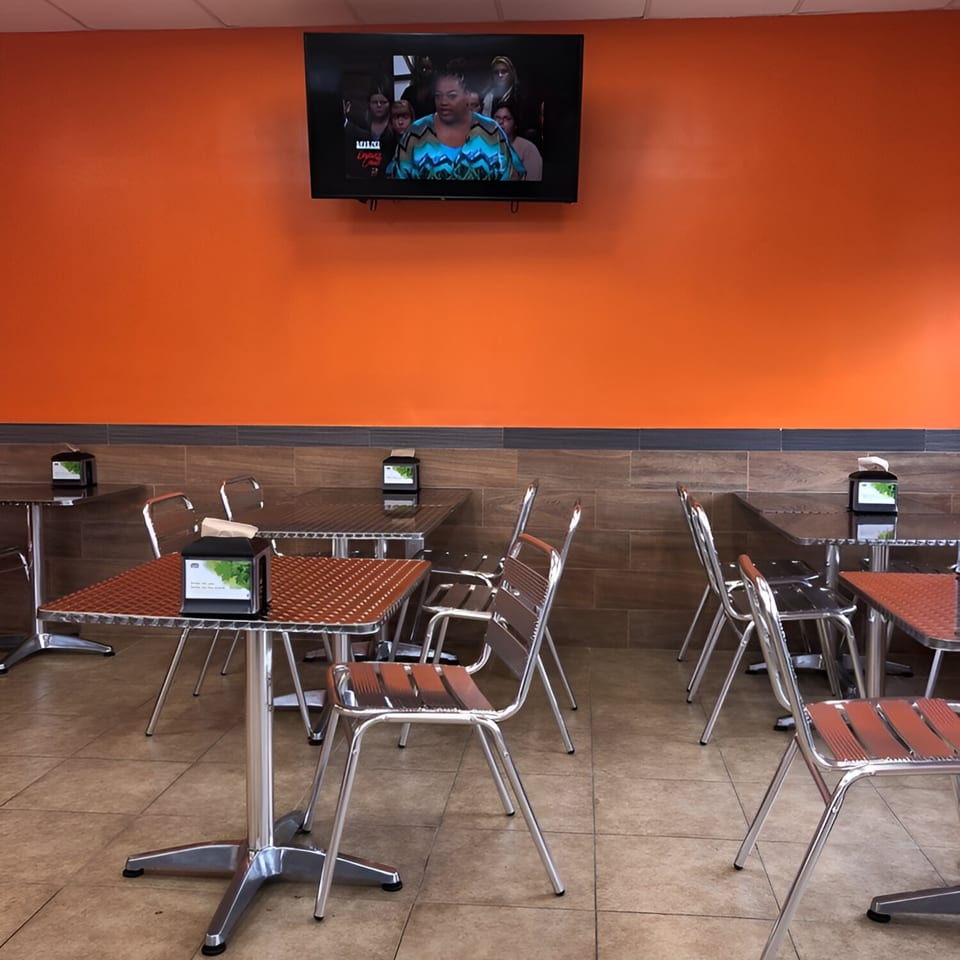 Empty Quickie’s Burgers, Wings & Seafood dining area with orange walls, metal tables, and chairs.