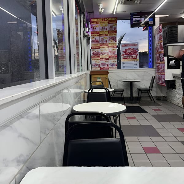 Interior of Quickie's Burgers, Wings & Seafood, showing empty tables, chairs, and menu boards.