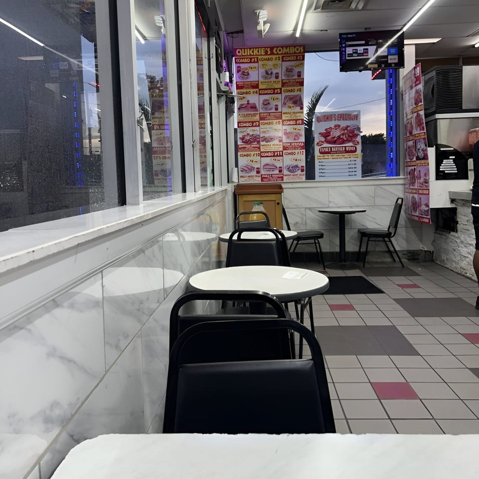 Interior of Quickie's Burgers, Wings & Seafood, showing empty tables, chairs, and menu boards.