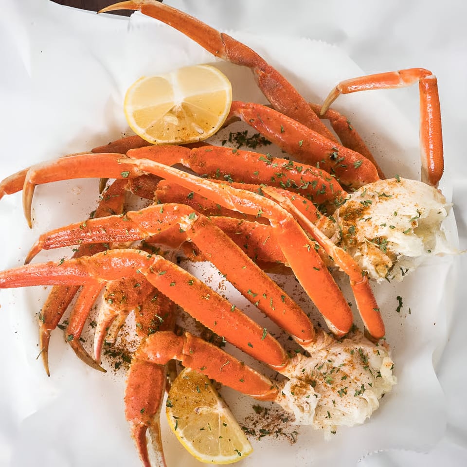 Quickie’s Burgers, Wings & Seafood snow crab legs with lemon wedges and seasoning on white paper.