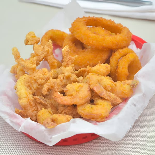 A red basket filled with crispy fried shrimp, clams, and golden onion rings.