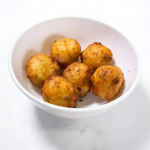 Six golden-brown hush puppies, a seafood side, are served in a white bowl.