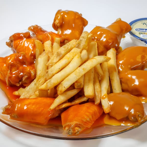 Quickie’s Burgers, Wings & Seafood's buffalo wings and french fries on a clear plate.